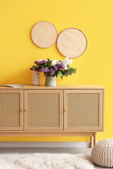 Vase with flowers on stylish cabinet near yellow wall in room