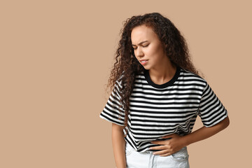 Young African-American woman with stomach ache on beige background