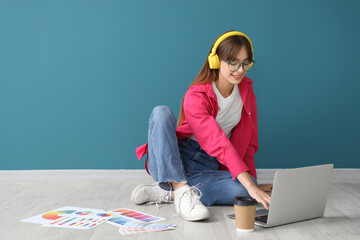 Female graphic designer in headphones working with laptop near blue wall