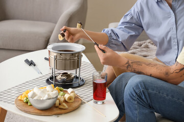 Young couple with glasses of wine dipping fresh bananas into chocolate fondue at home, closeup