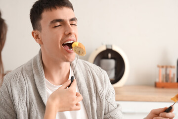 Young happy couple eating croutons dipped in cheese fondue at home