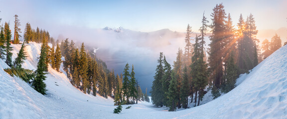 Snow covered rim of Crater Lake and Wizzard Island in Crater Lake National Park, Oregon. A panoramic cliff-side overview of deep blue Crater Lake, surrounded by the rugged lake rim, on a calm Spring 