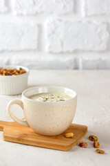 Vegan green matcha tea mixed with coconut milk and pistachio in latte cup on table. Vertical orientation.