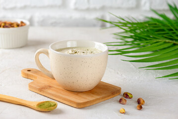 Pistachio green tea matcha latte with milk in a cup with palm branch on a light table.