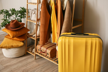 Rack with clothes and packed suitcase near beige wall in room, closeup