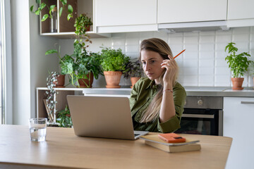 Pensive exhausted woman work on laptop studying online with books and water glass at home....