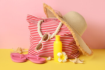 Wicker bag, bottle of sunscreen cream and beach accessories on color background, closeup