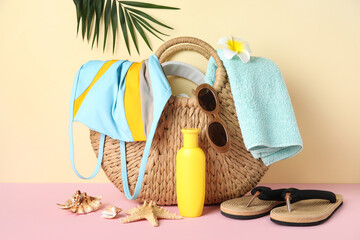 Wicker bag with swimsuit, bottle of sunscreen cream and beach accessories on color background,...