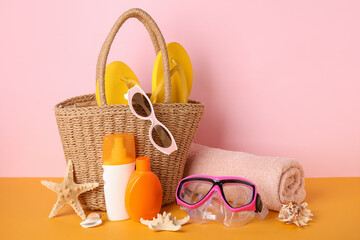Bag, bottles of sunscreen cream and beach accessories on color background, closeup