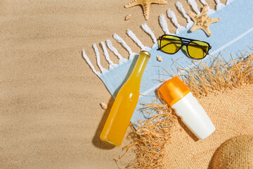 Summer composition with bottle of sunscreen cream, bottle of juice and beach accessories on sand as...
