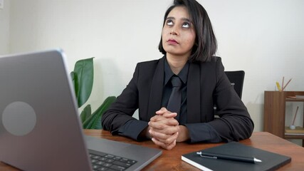 Woman in a black suit sitting attentively at her desk, focused on a video call interview via laptop