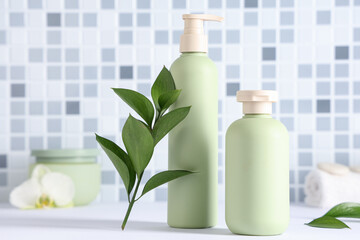Composition with bottles of shower gel and green twig on table near blue tile wall, closeup