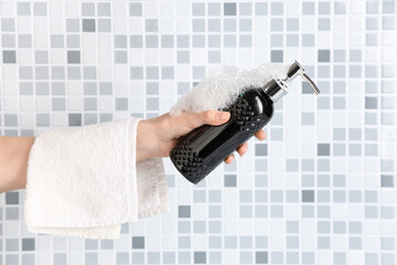 Female hand with bottle of shower gel, towel and foam on grey tile background