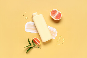 Composition with bottle of shower gel, grapefruit and cream smears on yellow background