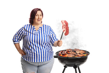 Chubby woman holding a fork with a raw steak in front of a bbq