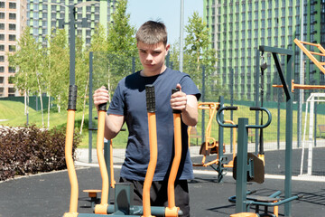 Focused young man training on outdoor fitness machine at modern city playground. Sport, health,...