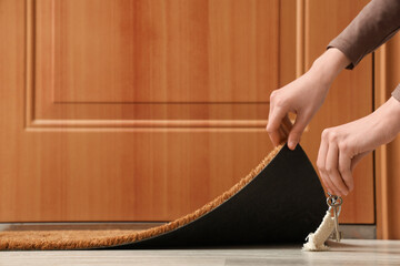 Woman putting key from house under door mat