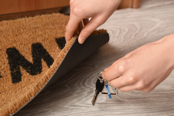 Woman putting key from house under door mat