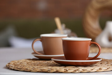 Cups of hot coffee on white table in room
