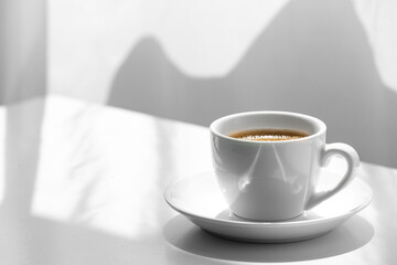 Cup of hot coffee on white table in room