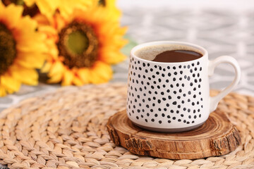 Cup of hot coffee and beautiful sunflowers on table, closeup
