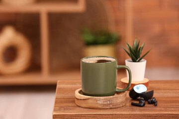 Cup of hot coffee and modern earphones on wooden table in room