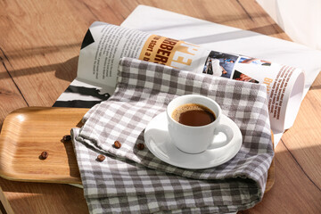 Cup of hot espresso with coffee beans and magazine on wooden table, closeup