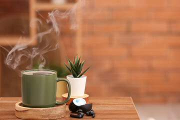 Cup of hot coffee and modern earphones on wooden table in room