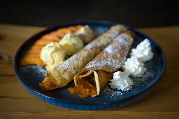 Delicious homemade sweet dessert - pancakes with apricot jam, ice cream, apricot slices, whipped cream, served on a blue platte