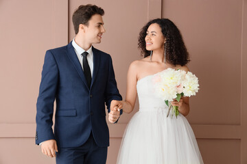 Young wedding couple holding hands near brown wall