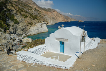 Seaside White Chapel with Blue Door and Bell Tower on Rugged Mediterranean Coastline, Greece