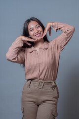 An Indonesian woman smiling joyfully while striking a playful pose with her hands on her face. Her...