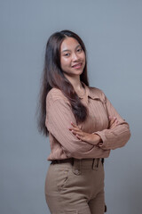 Portrait of a confident young Indonesian woman smiling with arms crossed, wearing a brown blouse...