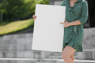 Young woman pointing at blank poster on city street