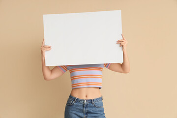 Young woman holding blank poster on beige background