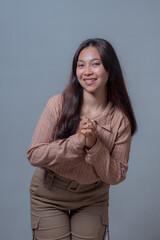 Portrait of a smiling young Indonesian woman bending slightly forward with hands clasped in front....
