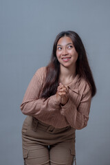 Young Asian woman from Indonesia smiling playfully while looking to the side, with her hands...