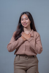 A young Indonesian woman smiling gently with a joyful expression, placing her hands on her chest in...