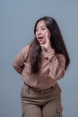 Young Indonesian woman in a beige shirt with an expressive face, standing and holding her hand to...