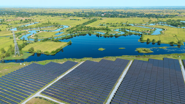 Drone shot aerial view solar energy array provides renewable power in large scale facility surrounded by greenery and water in rural place. Solar farm at the countryside