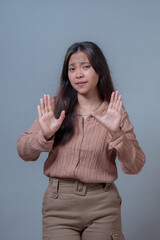 An Asian woman in a beige shirt and pants, holding both hands up with open palms, showing a 