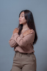 An Indonesian woman in a beige blouse standing with arms crossed, looking confidently to the side....