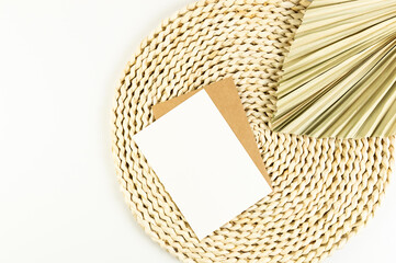 Top view of brown wicker table mat, dried palm leaf on white background. White and brown cards,...