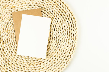 Top view of brown wicker table mat, white and brown cards on white background. Straw round tray, flat lay, copy space. 