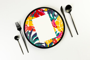 Top view of black tray, colorful plate, black cutlery on white background. White card, exotic plant plate, summer picnic. Flat lay, copy space.