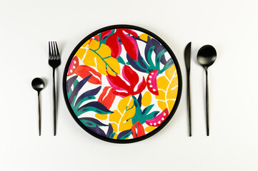Top view of black tray, colorful plate, black cutlery on white background. Exotic plant plate,...