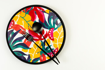 Top view of black tray, colorful plate, black cutlery on white background. Exotic plant plate, summer picnic. Flat lay, copy space.