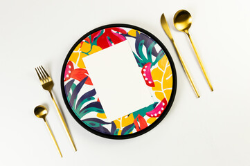 Top view of black tray, colorful plate, gold cutlery on white background. White card, exotic plant plate, summer picnic. Flat lay, copy space.