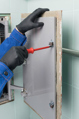 the master adjusts the hinges of the hidden door, water supply communications, using a screwdriver, close-up