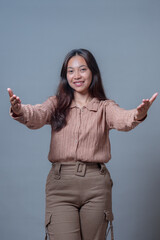 Portrait of a cheerful Indonesian woman with long hair smiling and extending both arms forward in a...